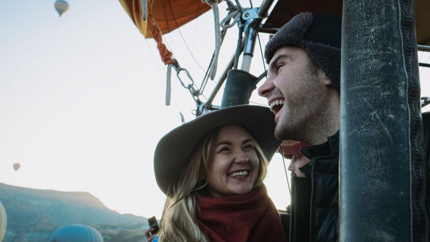 Two friends laughing in a hot air balloon basket at sunrise